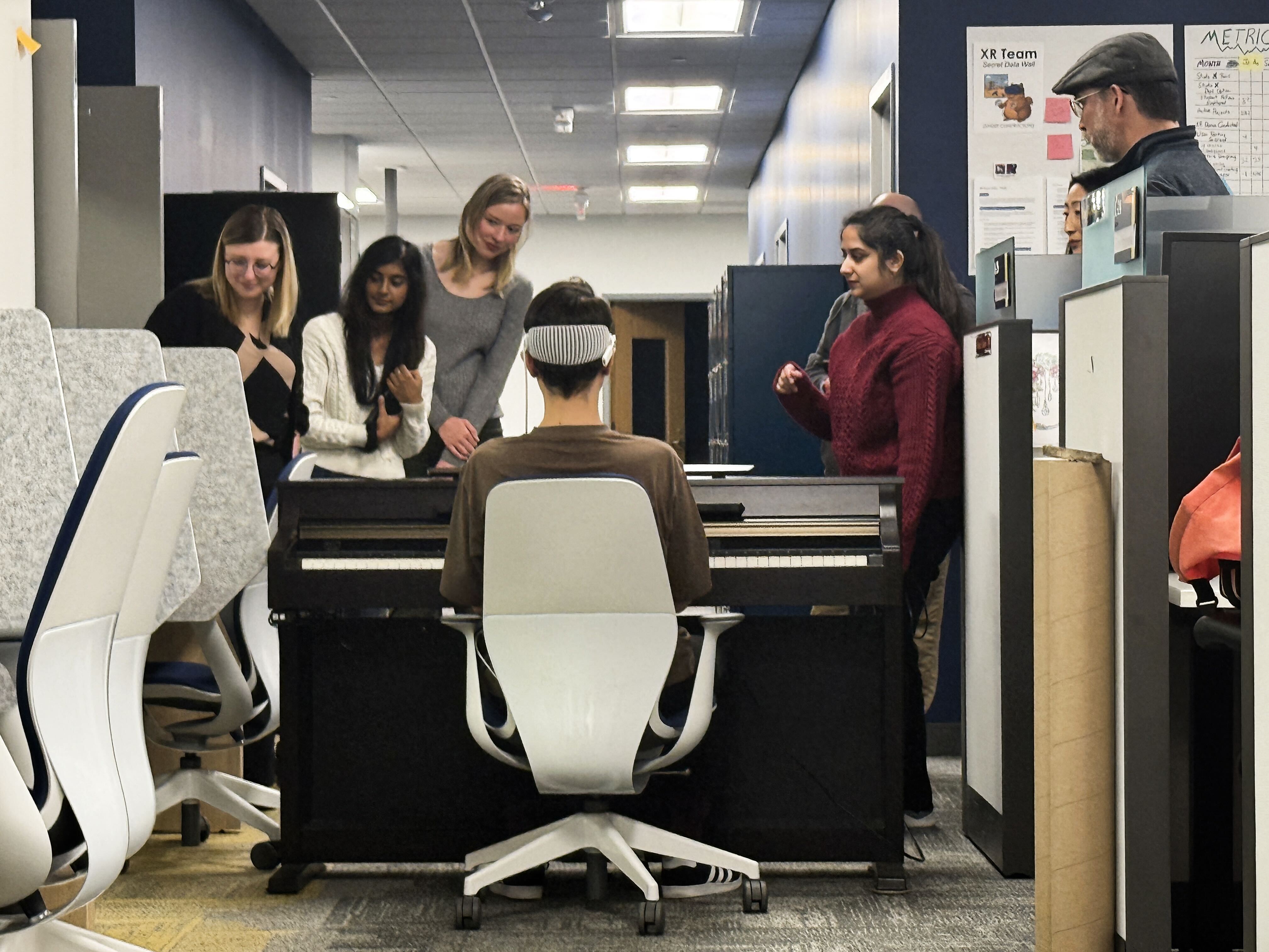 The whole team watching a participant try the app at the piano during a faculty headset test